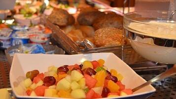 A buffet with various food items including a bowl of mixed fruits and several containers of dips.