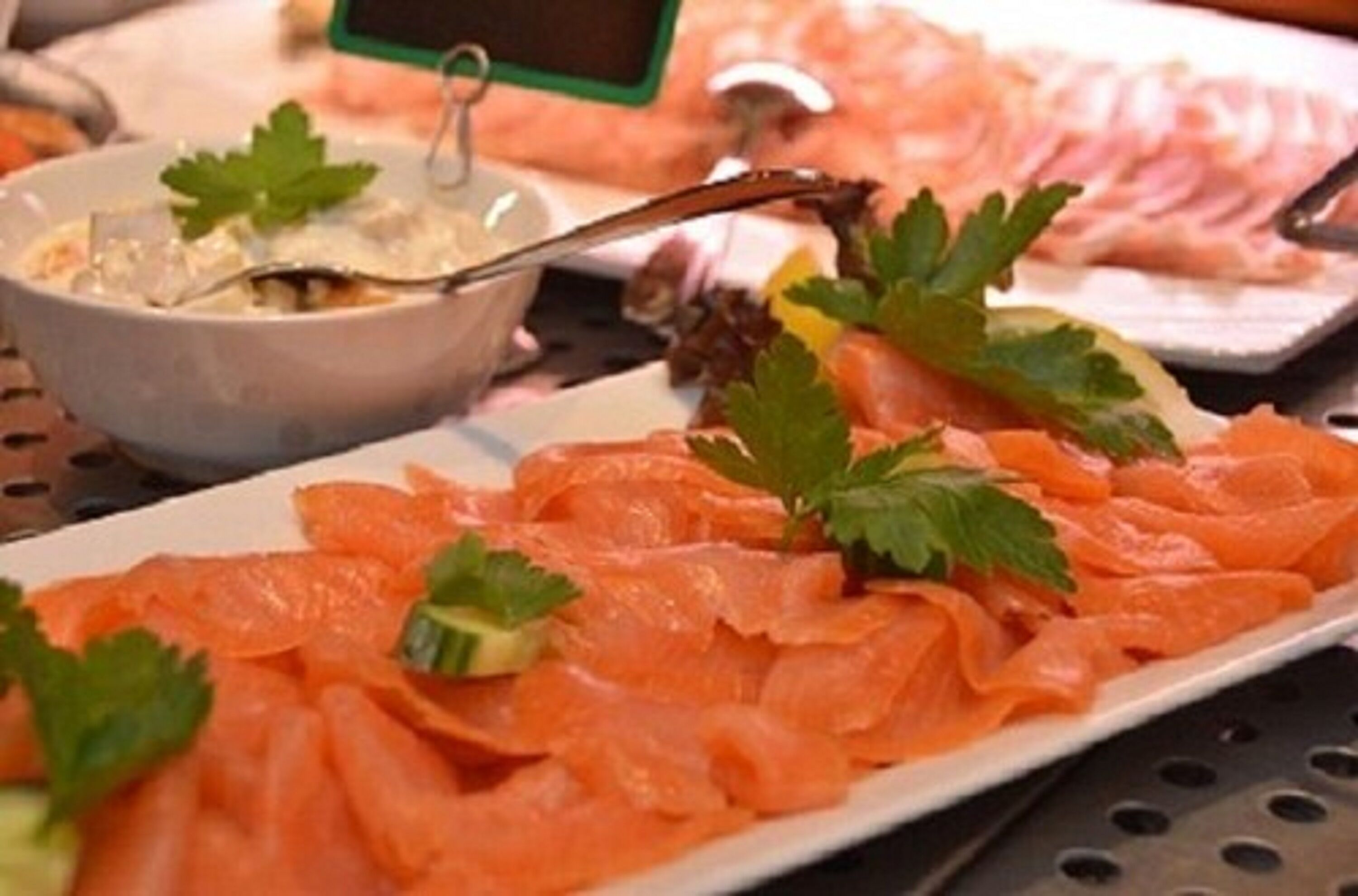 A plate of smoked salmon garnished with parsley, accompanied by a bowl of soup and a fork.