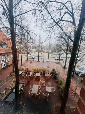 An outdoor seating area with tables and chairs, surrounded by trees and a brick pathway. - Hotel Diamant (Wedel)