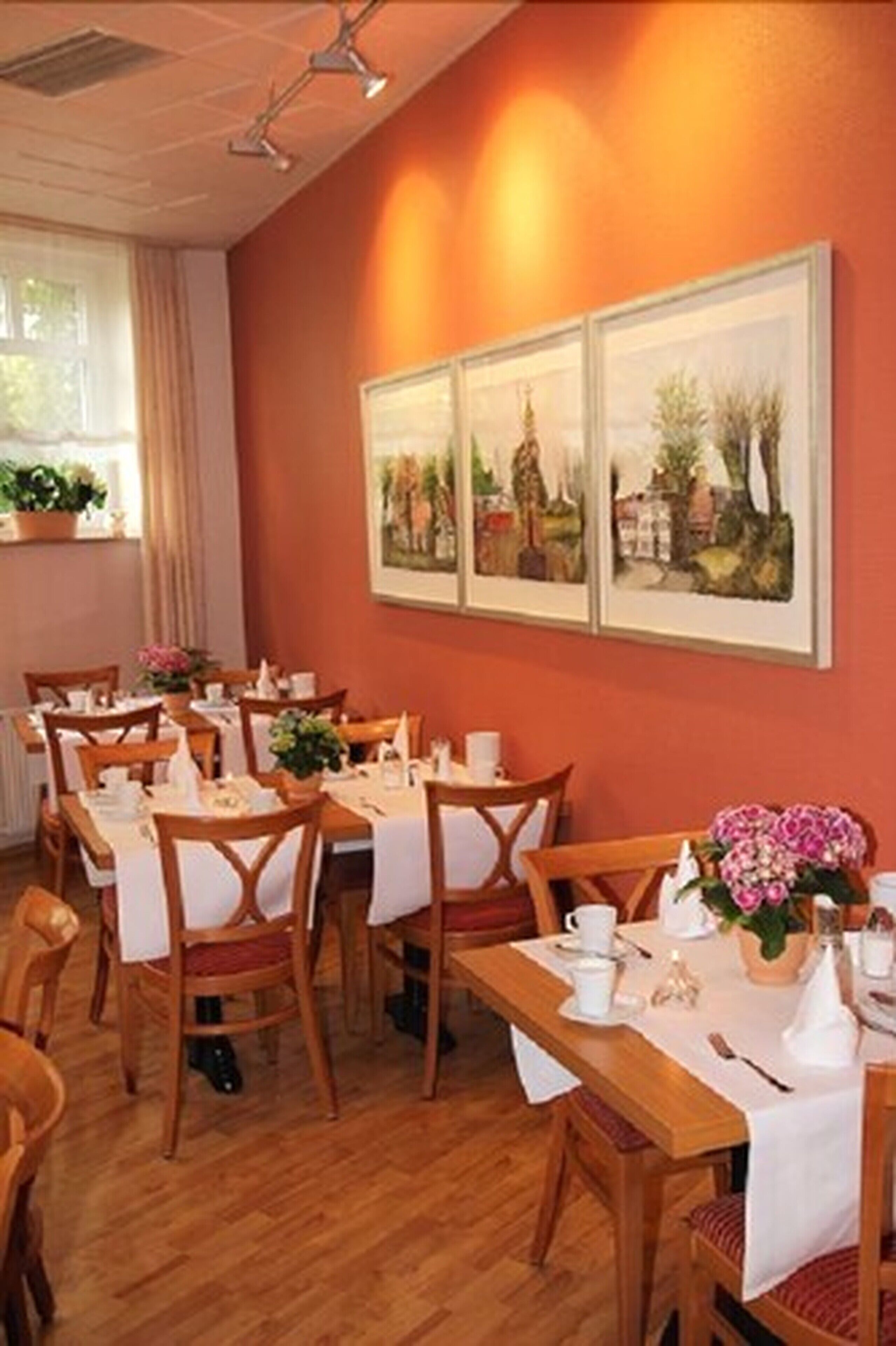 A dining area with wooden tables and chairs, white tablecloths, and potted plants.