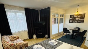 A hotel room with a bed, a sofa, a desk with chairs, a radiator, a window with curtains, and a wall with a word cloud. - Hotel Diamant (Wedel)