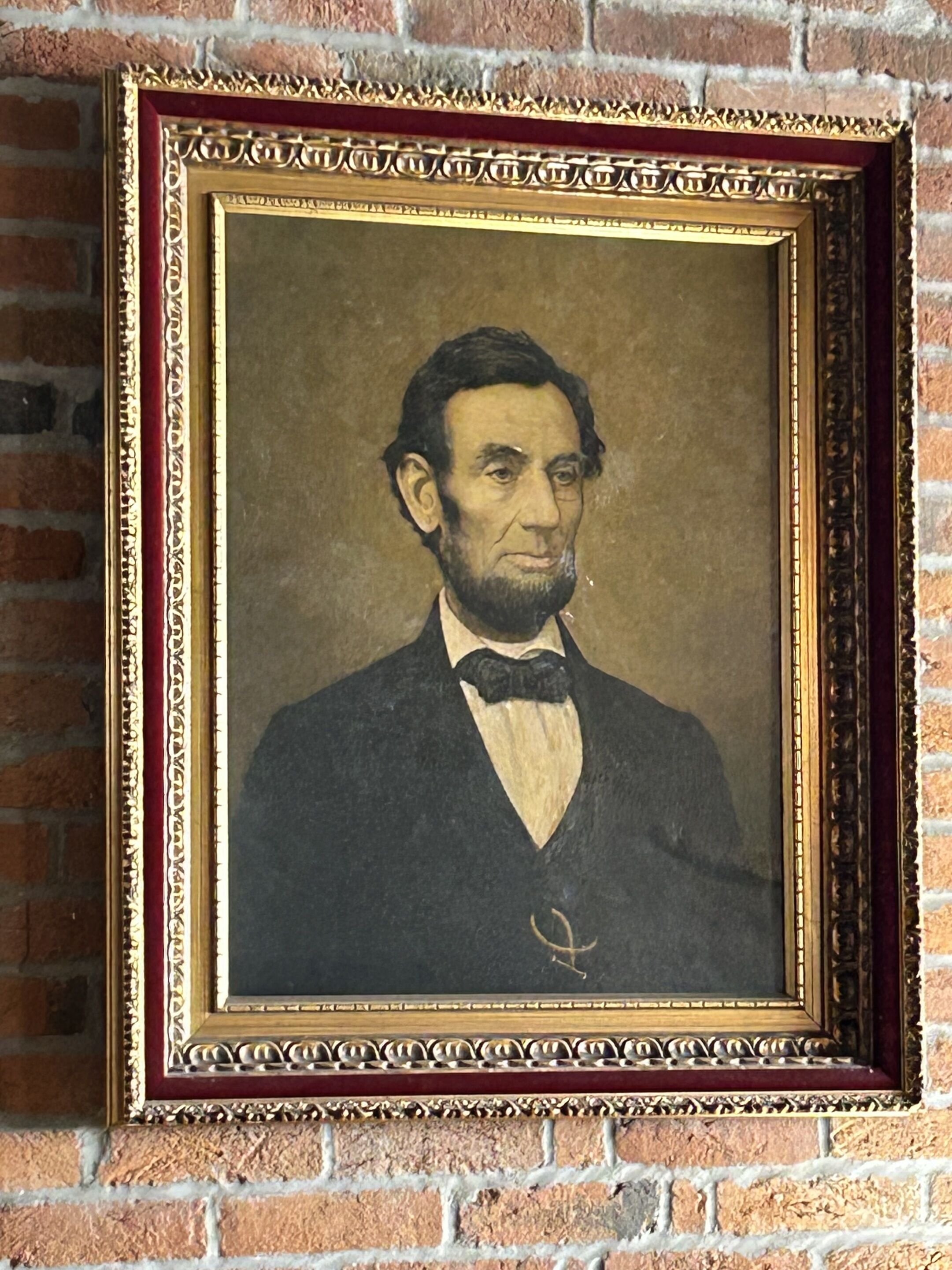 Retrato enmarcado de un hombre con traje y corbata de moño, frente a un muro de ladrillo.