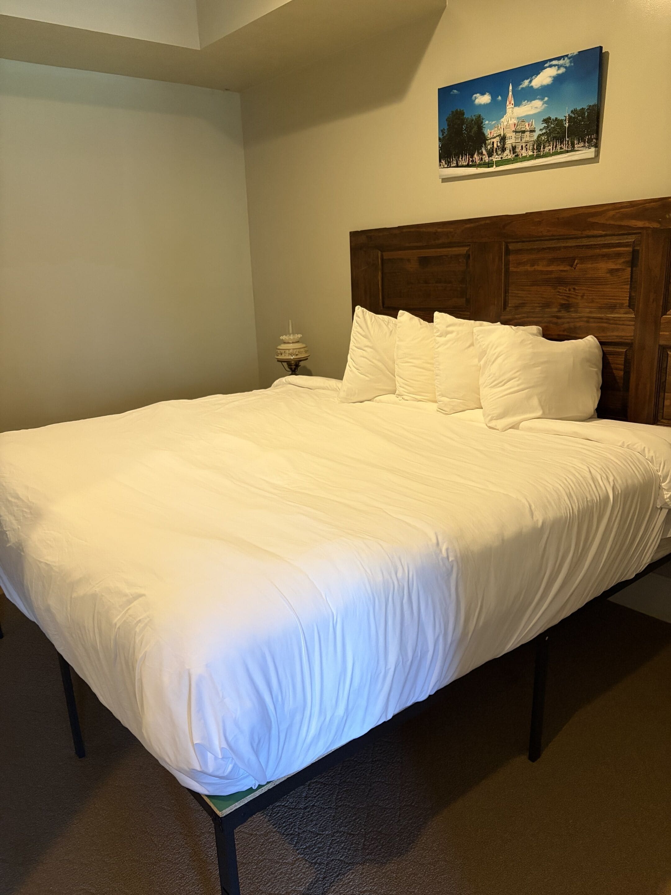 A neatly made bed with white linens in a room with a wooden headboard, a small bedside table, and a framed picture on the wall.