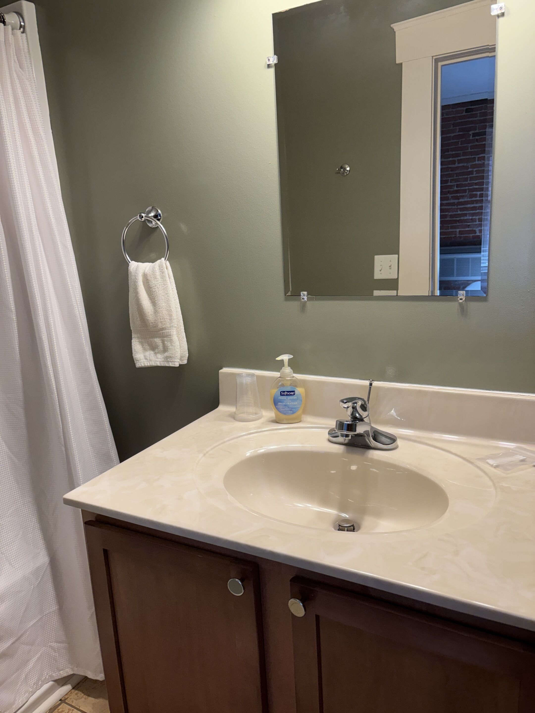 A bathroom with a white sink, a mirror, and a towel hanging on a ring.
