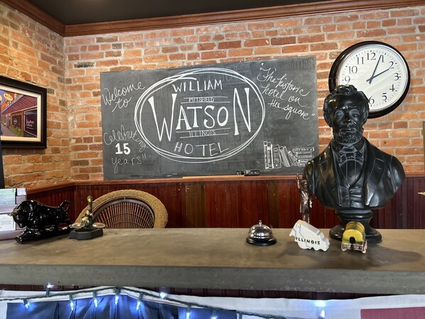 A hotel reception area with a chalkboard sign, a clock, and a bust of a historical figure.