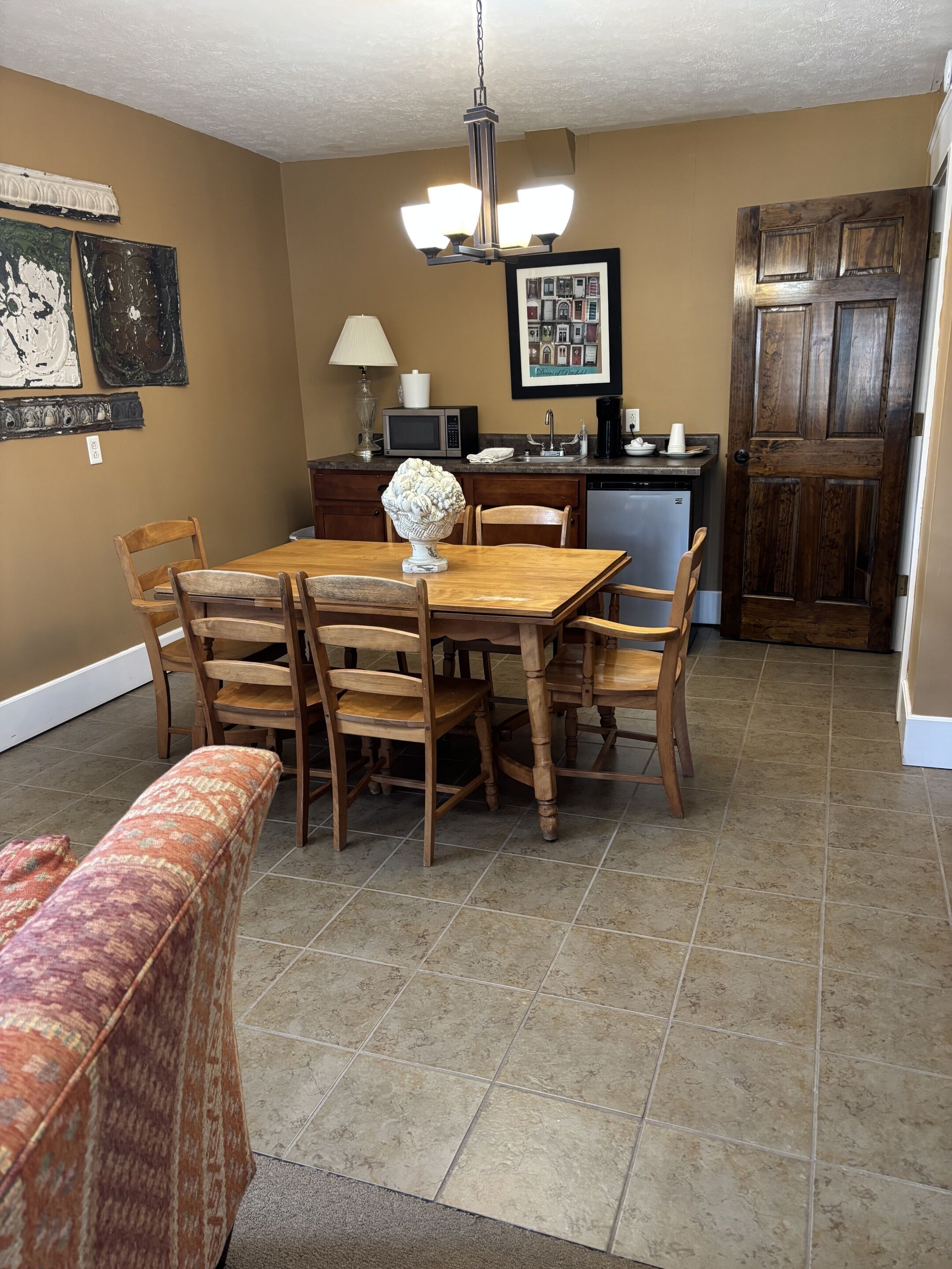 A dining area with a wooden table, chairs, a bench, a decorative bowl, a microwave, a coffee maker, and a framed picture on the wall.