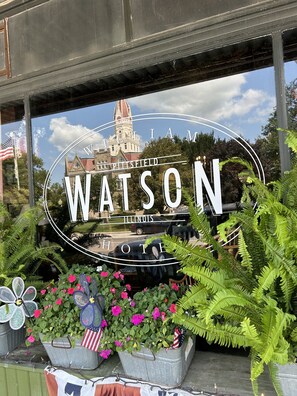 A sign with "WATSON" prominently displayed, surrounded by greenery and flowers.