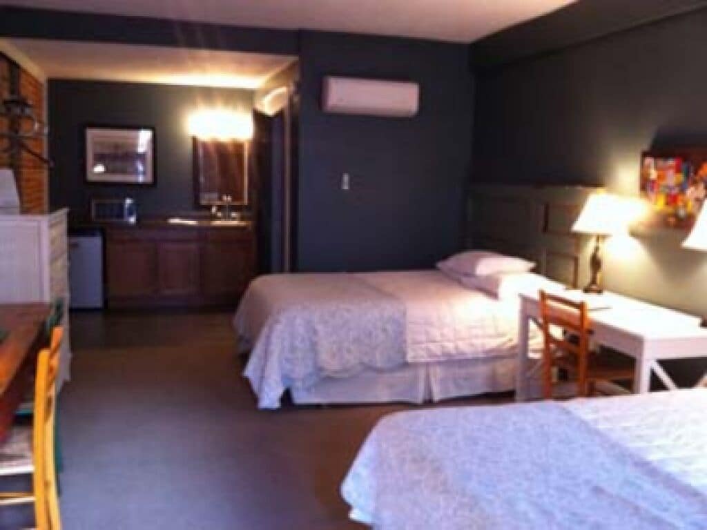 A hotel room with two beds, a desk, a chair, a small kitchenette, and a bathroom.