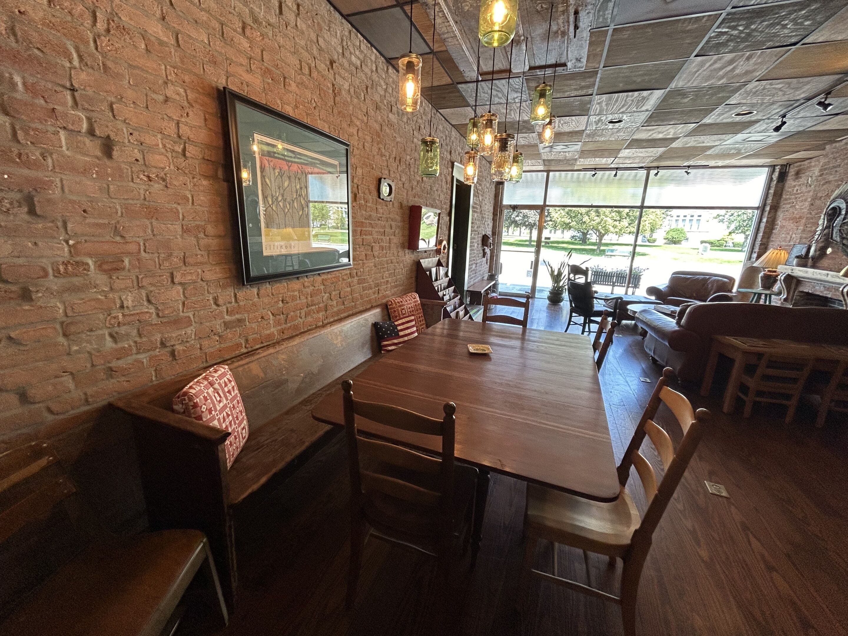 A restaurant with a long wooden table, brick walls, and hanging light fixtures.