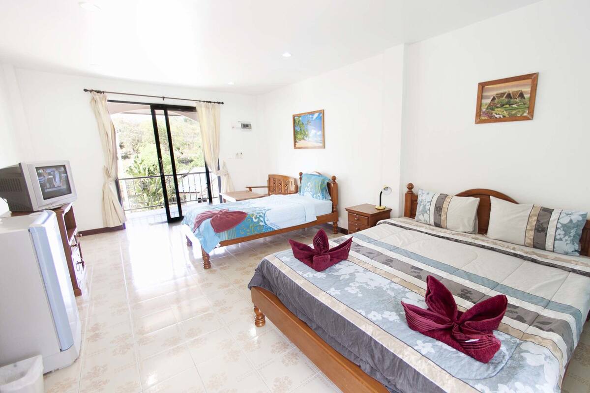 A hotel room with two beds, a TV, a desk, and a balcony.