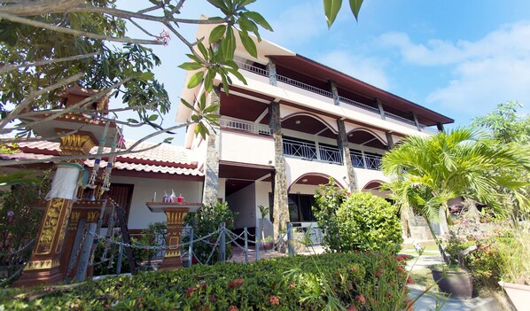 A multi-story building with a balcony, surrounded by lush greenery and a decorative fountain. - Lotus Friendly Hotel (Koh Samui)