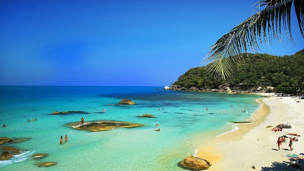 A beach with clear turquoise water, rocky formations, and a sandy shore with people. - Lotus Friendly Hotel (Koh Samui)