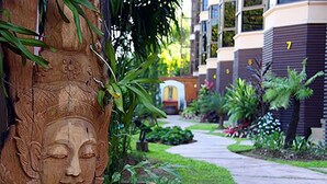 A pathway leading to a building with numbered doors, surrounded by lush greenery and a large carved tree. - Villa San Pee Seua (Chiang Mai)