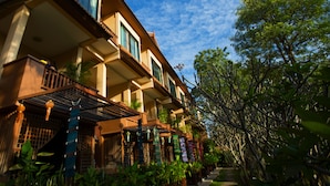 A multi-story building with balconies, a covered walkway, and lush greenery. - Villa San Pee Seua (Chiang Mai)
