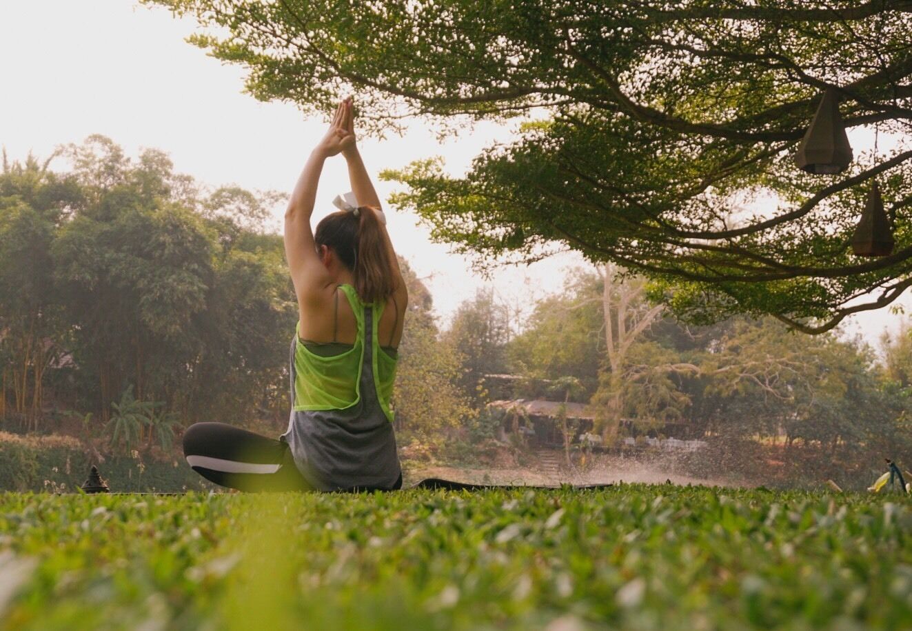 A person performing a yoga pose outdoors with trees and a clear sky in the background.