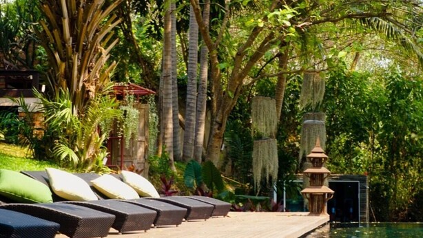 A poolside area with lounge chairs and a decorative water feature. - Villa San Pee Seua (Chiang Mai)