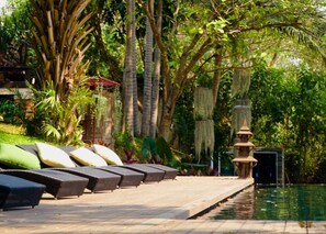 A poolside area with lounge chairs and a decorative water feature. - Villa San Pee Seua (Chiang Mai)