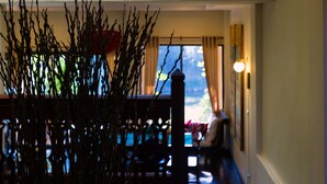 A room with a hanging woven light fixture, a view of the outdoors through a window, and a wooden railing with branches in the foreground. - Villa San Pee Seua (Chiang Mai)