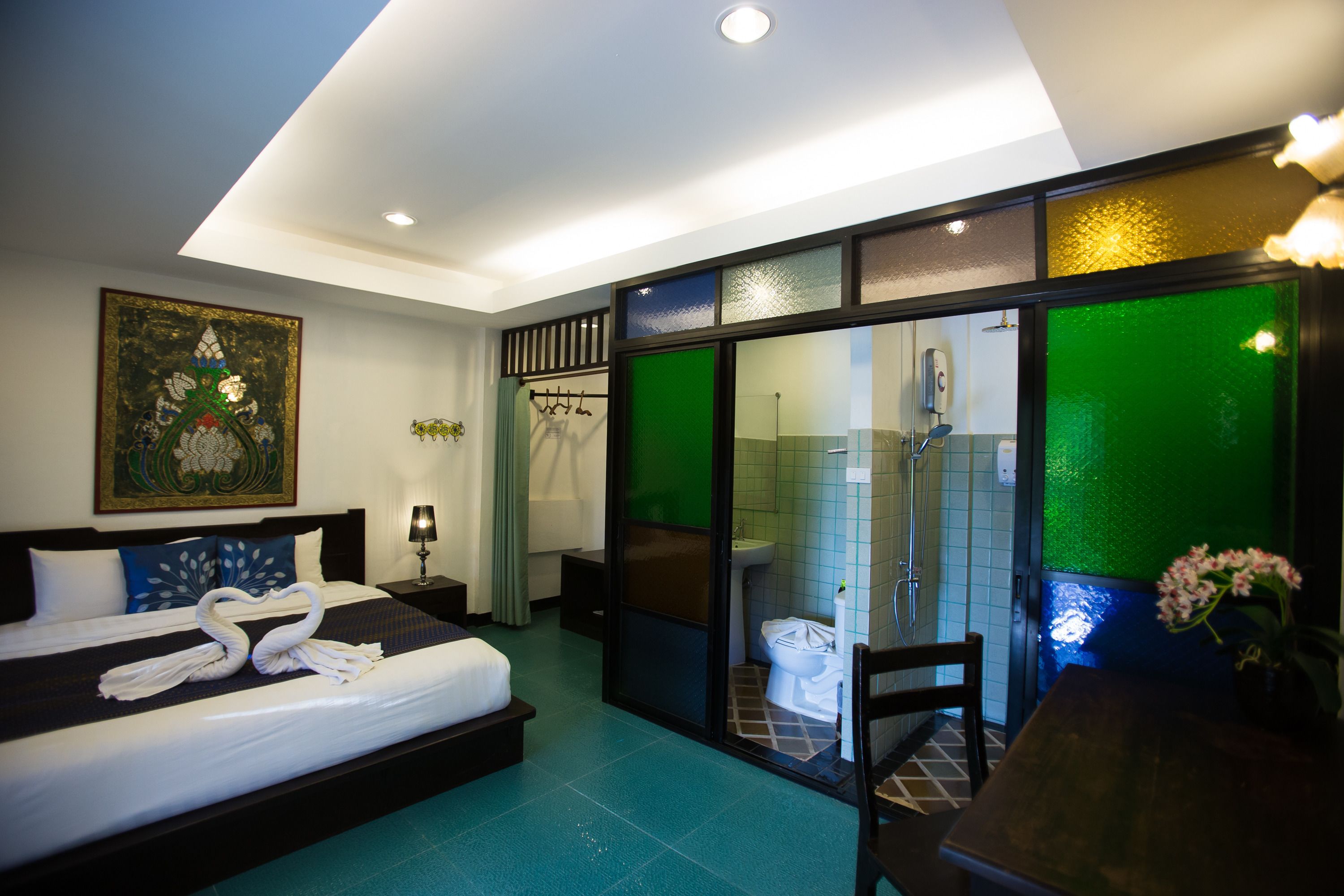A hotel room with a large bed, a desk, a chair, a bathroom with a glass shower enclosure, and a painting on the wall.