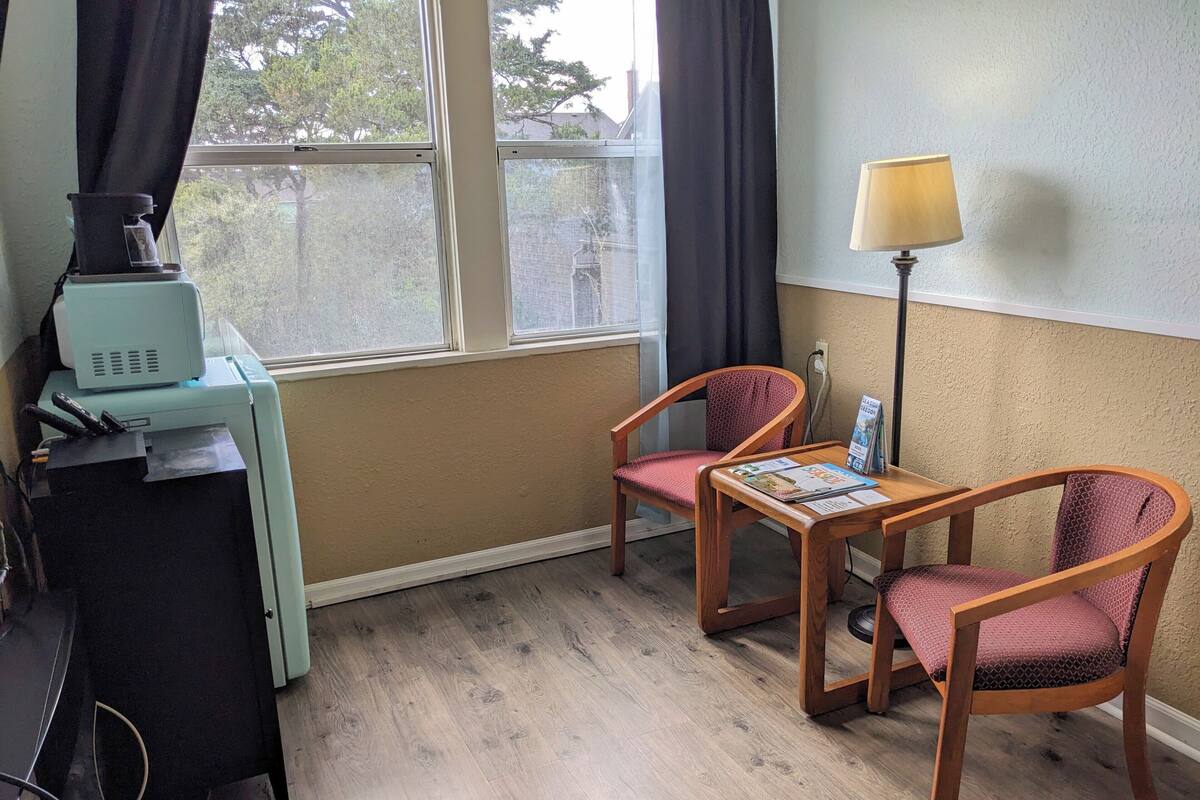 A room with a desk, two chairs, a lamp, and a window with curtains.