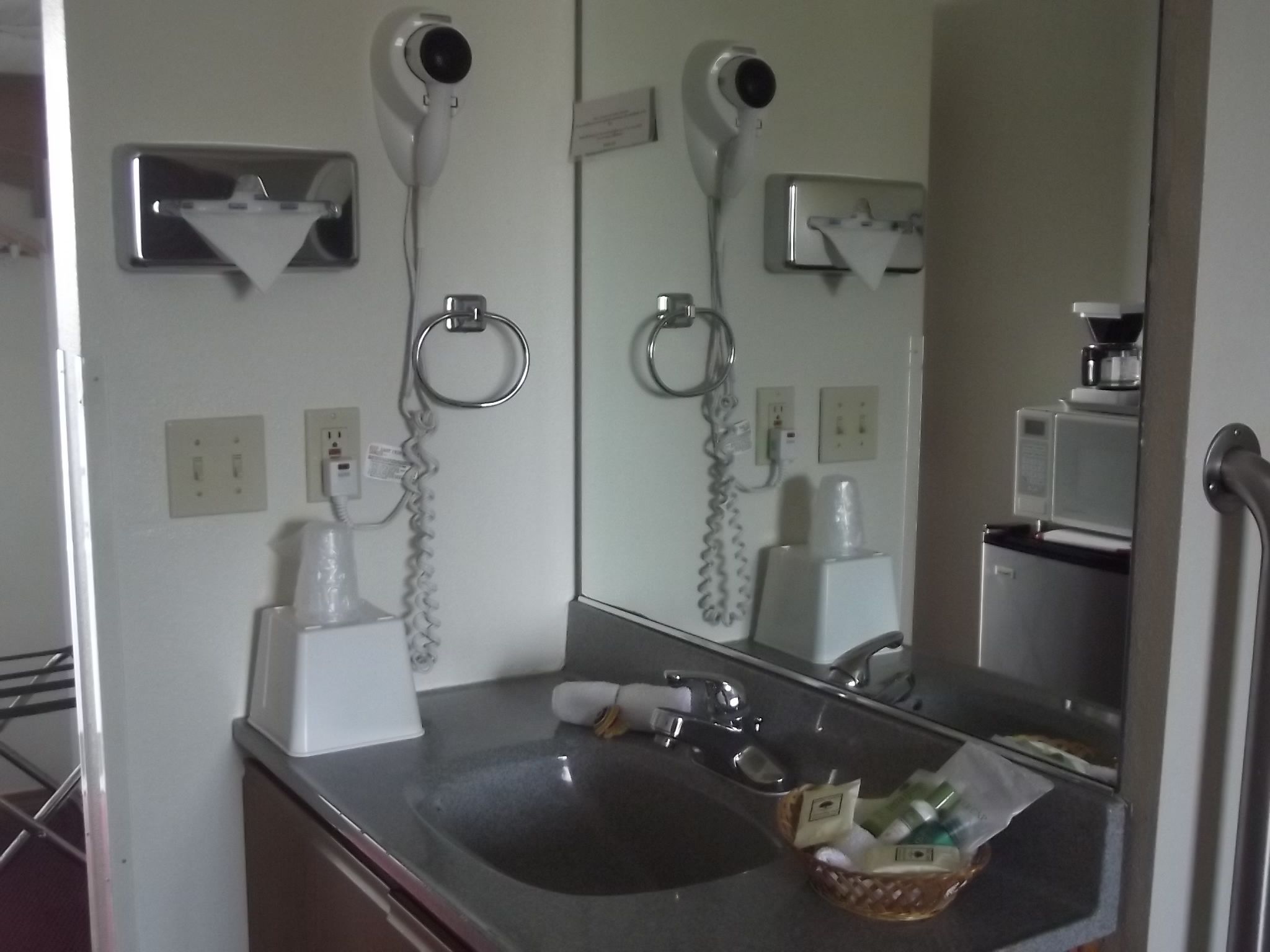 A bathroom with a sink, two hair dryers mounted on the wall, a mirror, and a coffee machine.