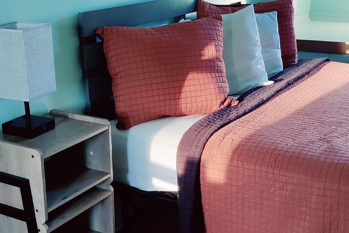 A bedroom with a bed, nightstands, a lamp, and a wall-mounted artwork.