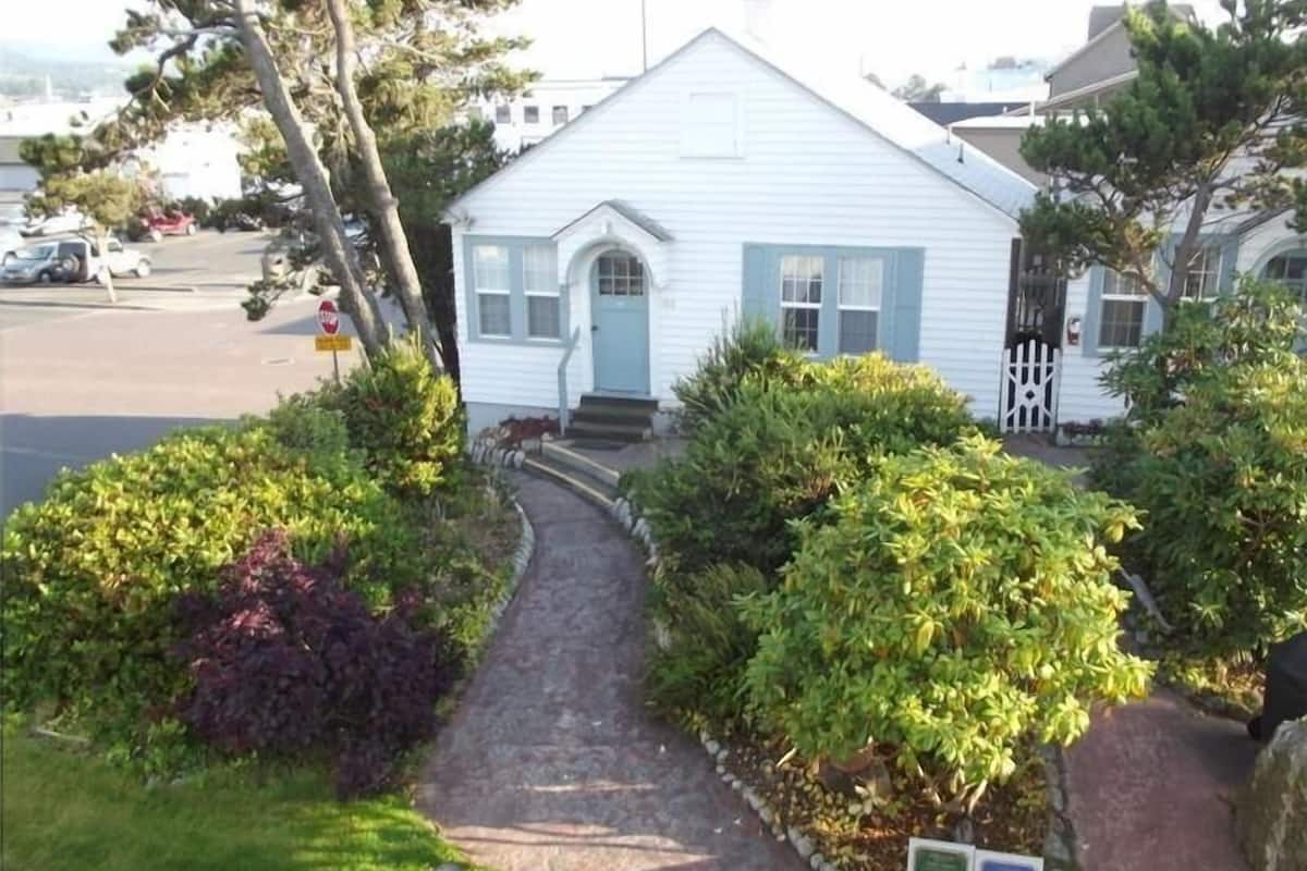 A white building with a blue door and windows, surrounded by well-maintained bushes and a paved path leading to the entrance.
