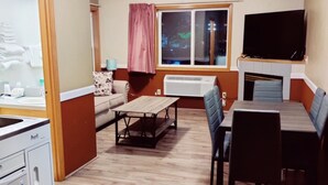 Un espacio habitable compacto con kitchenette, comedor y televisor sobre la chimenea.