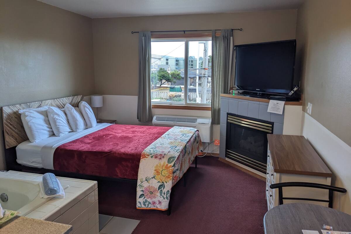 A hotel room with a bed, a desk, a television, a fireplace, and a window with curtains.