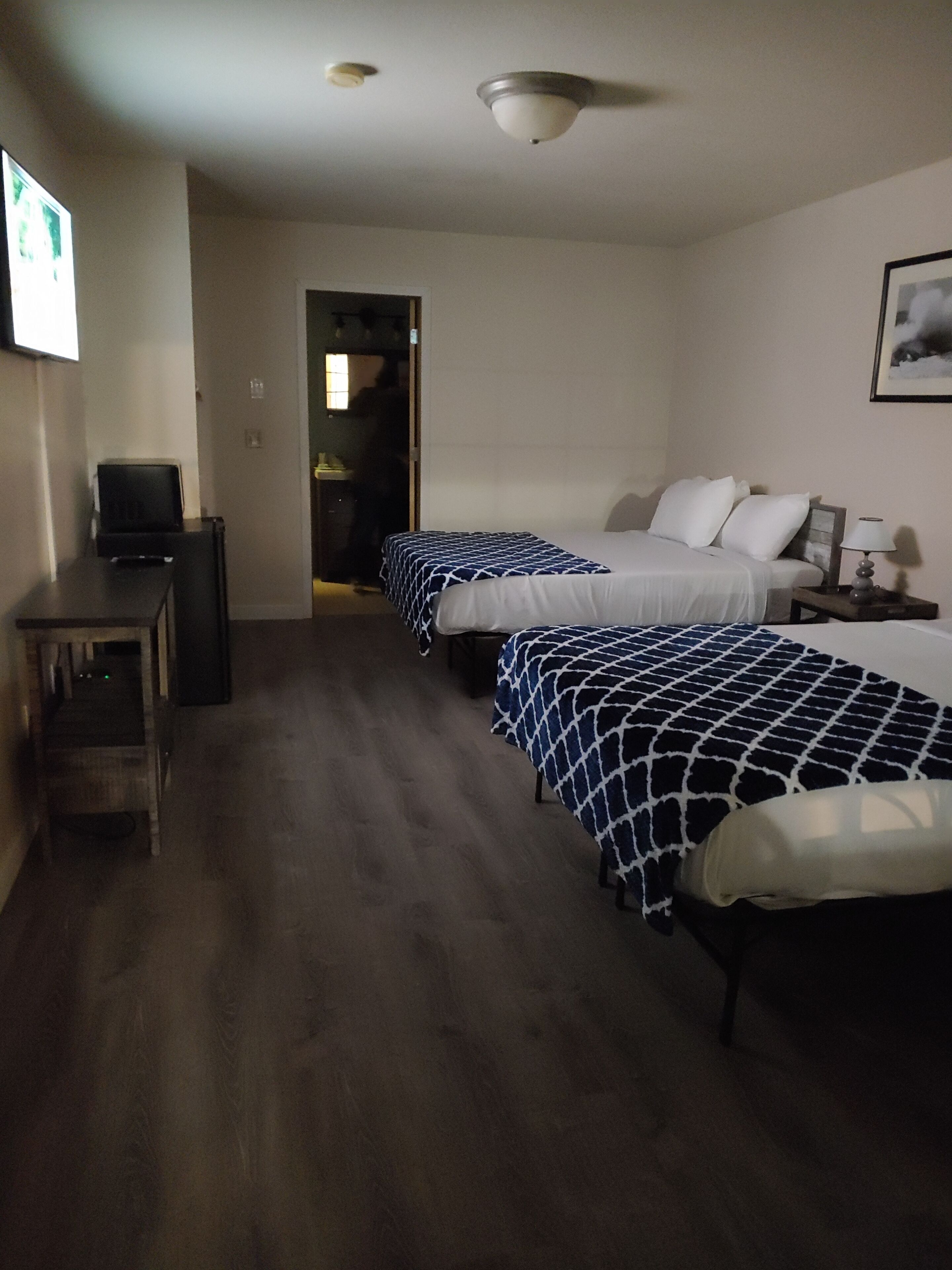 A hotel room with two beds, a desk, a television, and a ceiling fan.