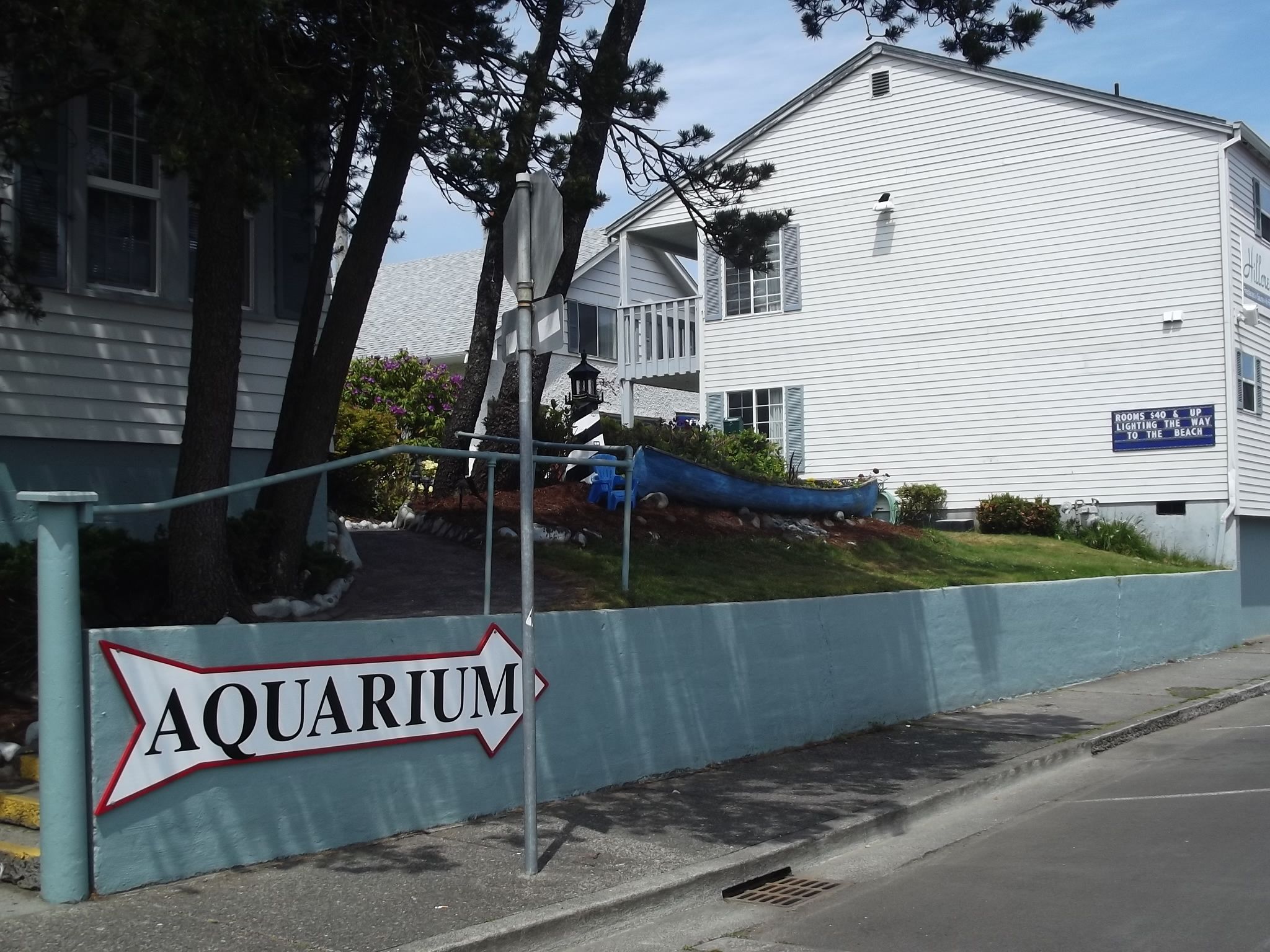 A sign for an aquarium with a white building in the background.