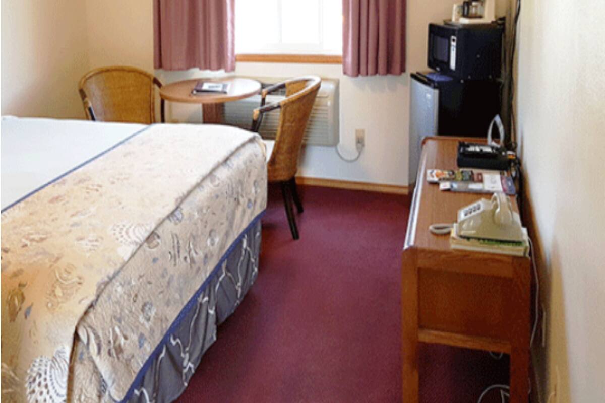 A hotel room with a bed, a desk, a chair, a television, and a window with curtains.