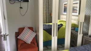 Un dormitorio con cama, una silla, armario y televisor fijado a la pared.