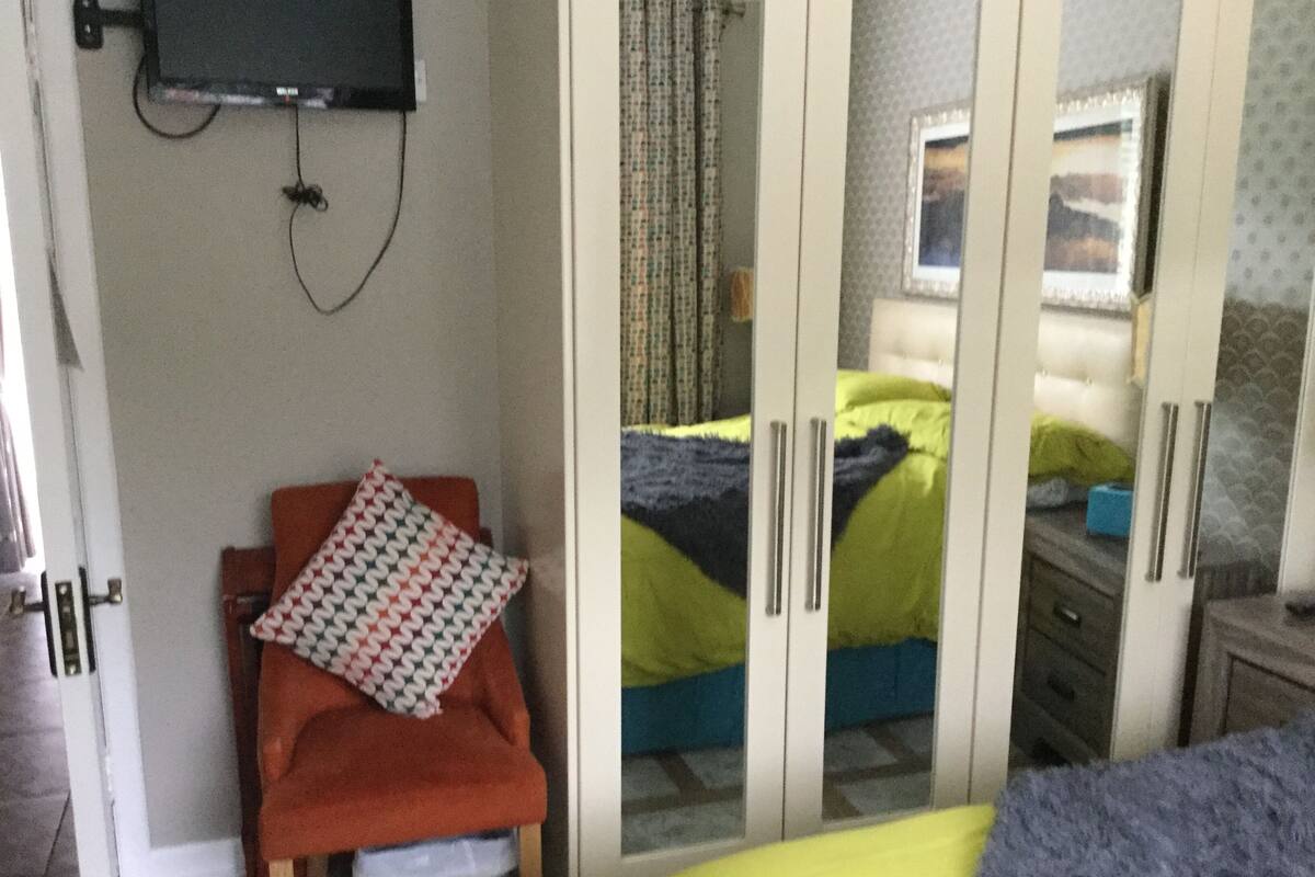 A bedroom with a bed, a chair, a wardrobe, and a television mounted on the wall.