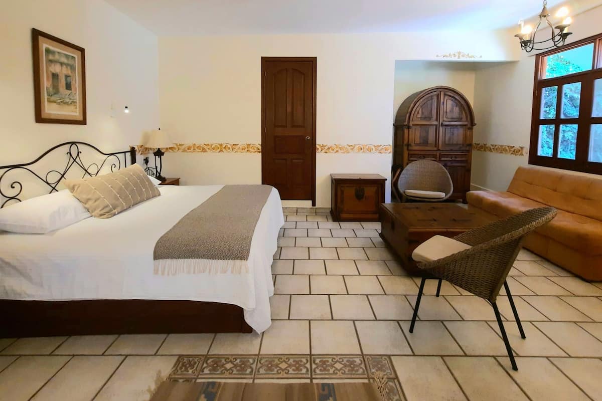 A bedroom with a bed, a nightstand, a dresser, a chair, and a sofa.