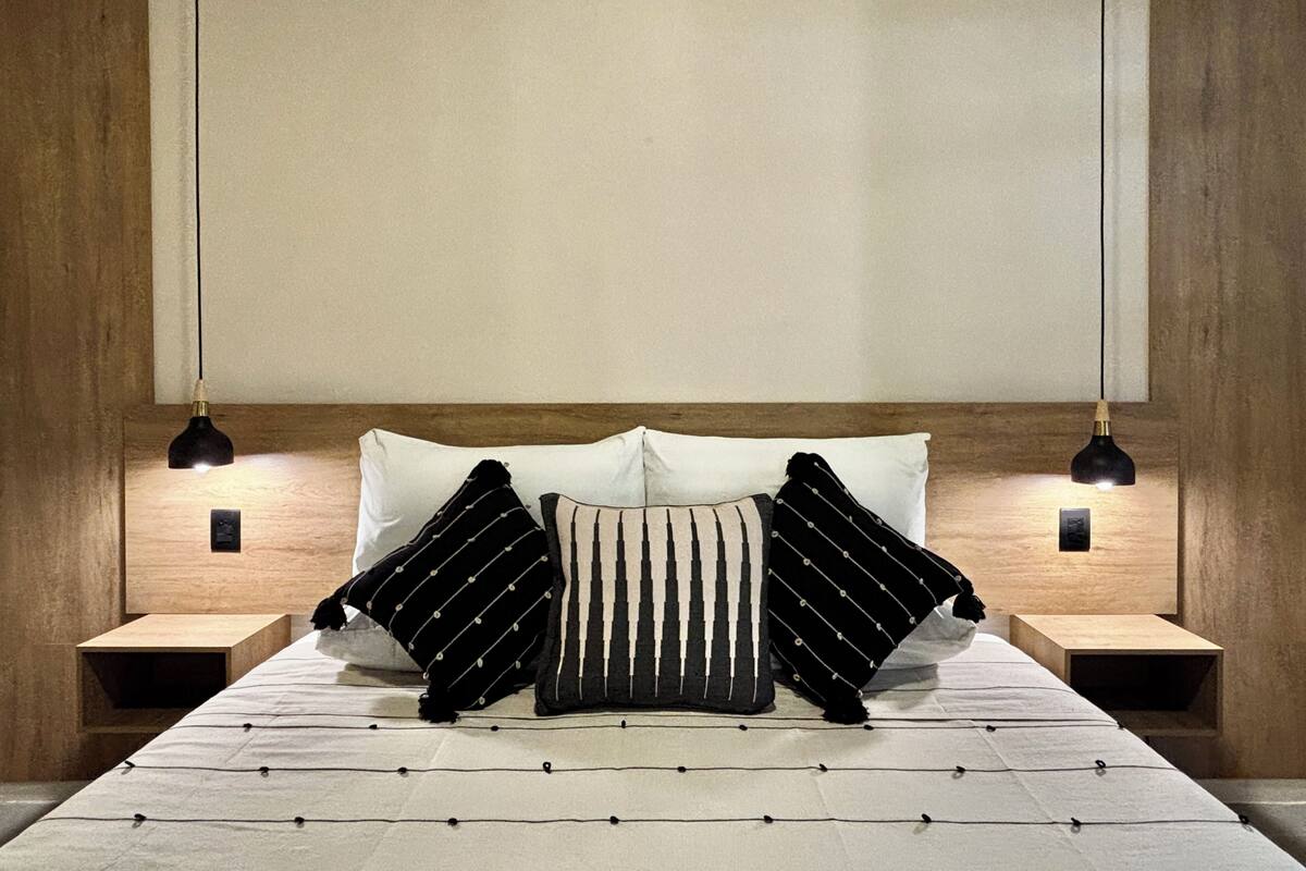 A neatly made bed with a white and black striped pillow, two black lamps, and wooden headboard and nightstands.