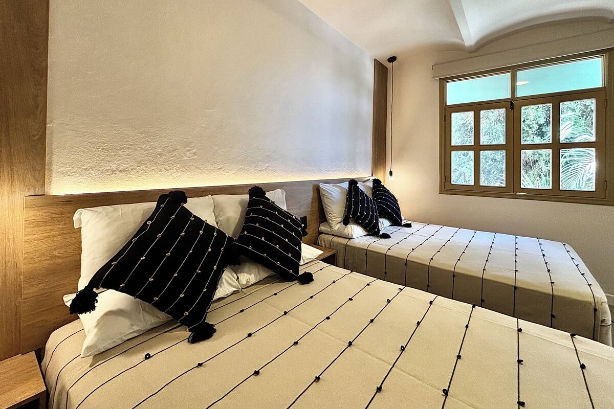 A bedroom with a large bed, a smaller bed, and a window with a view of trees.