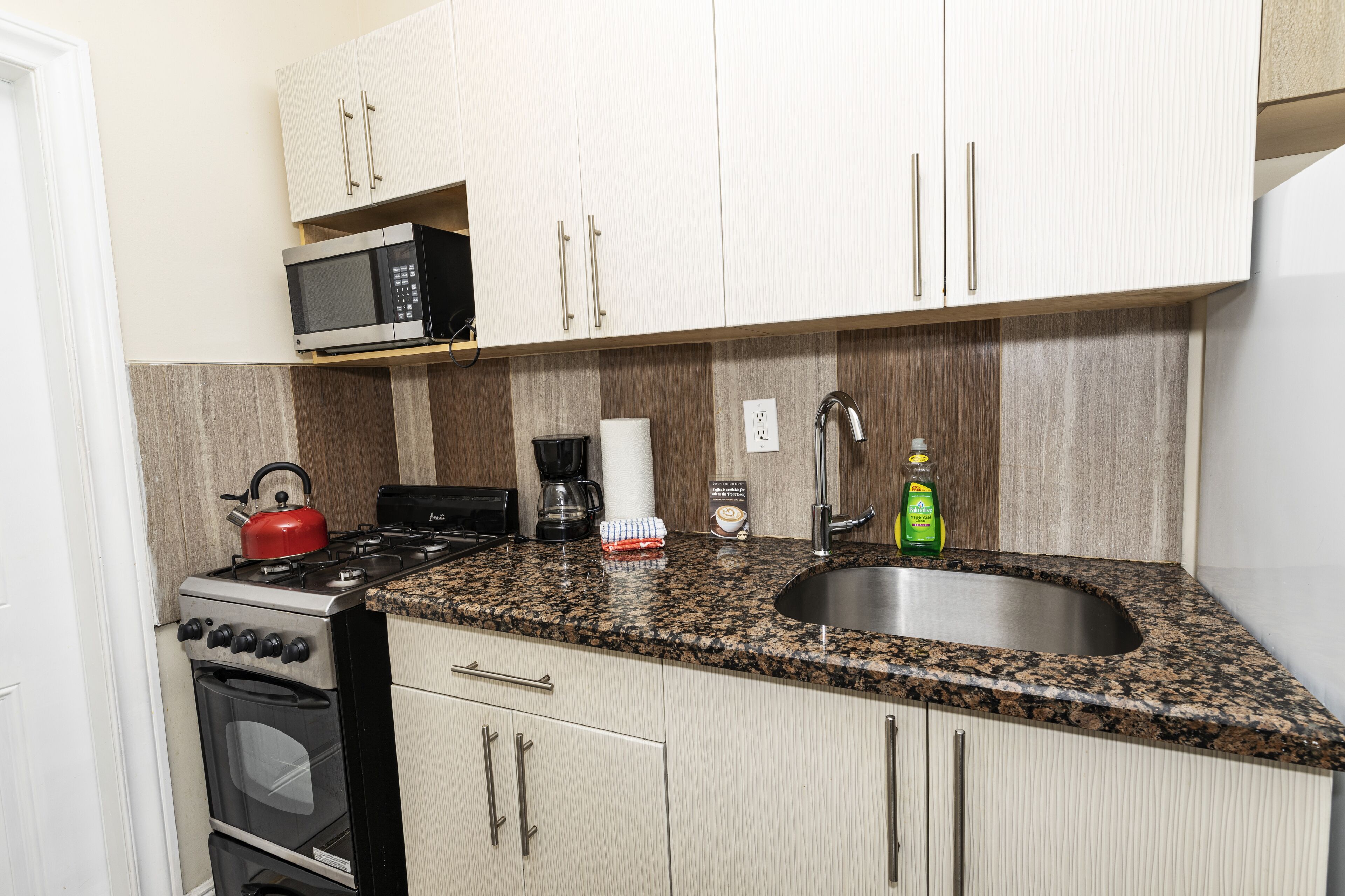 A kitchen with a granite countertop, stainless steel sink, microwave, stove, and oven.