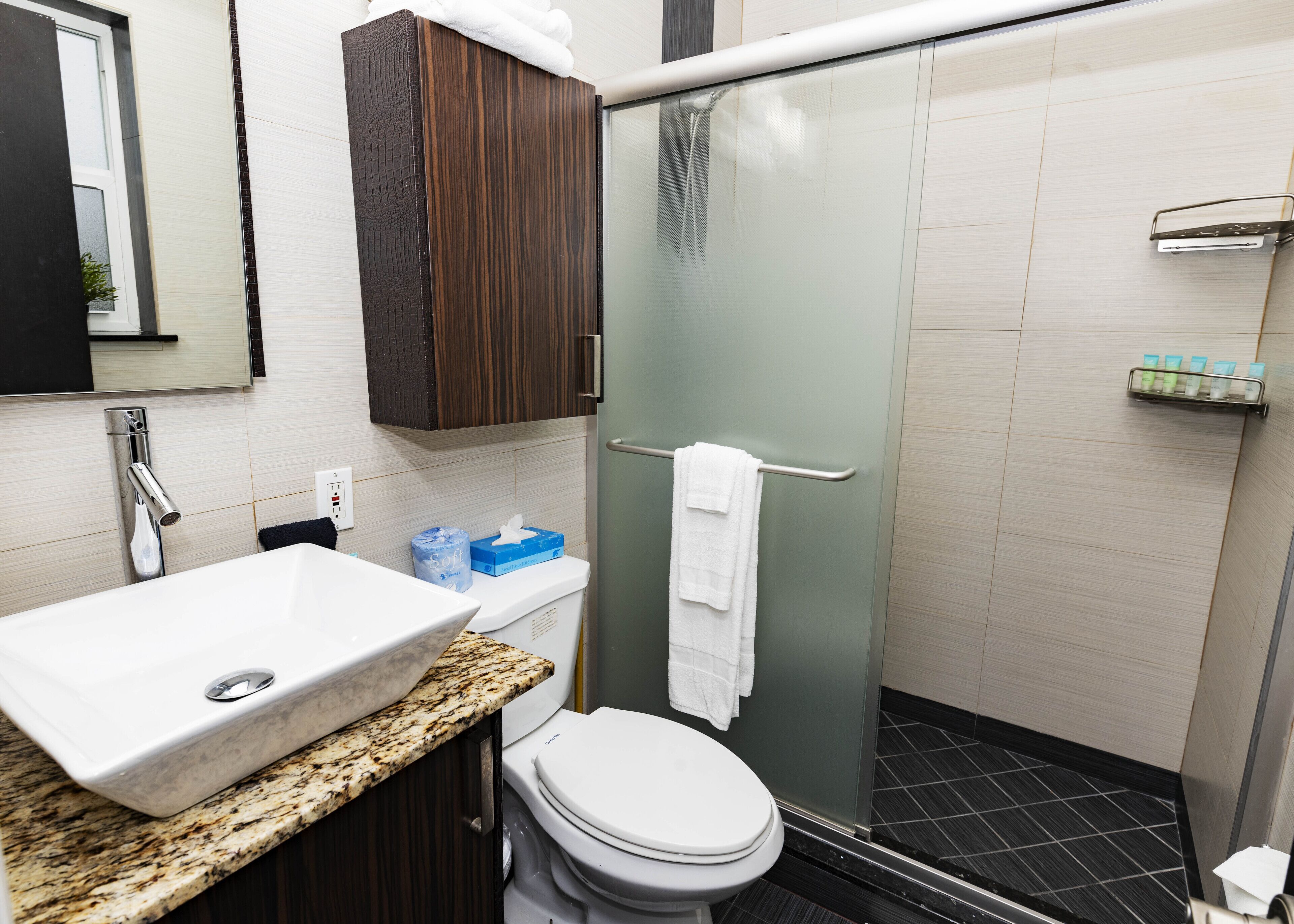 Un bagno moderno con lavabo in marmo, un water, box doccia in vetro e mobile contenitore in legno.
