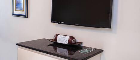 Un téléviseur à écran plat fixé au mur, un tableau encadré au-dessus, et un objet décoratif posé sur un comptoir.