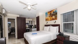 A hotel room with a bed, a desk, a chair, a ceiling fan, and a painting of a sunset.
