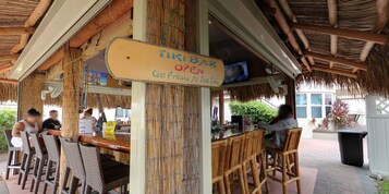 A tiki bar with a thatched roof, bamboo furniture, and a sign advertising the bar as open.