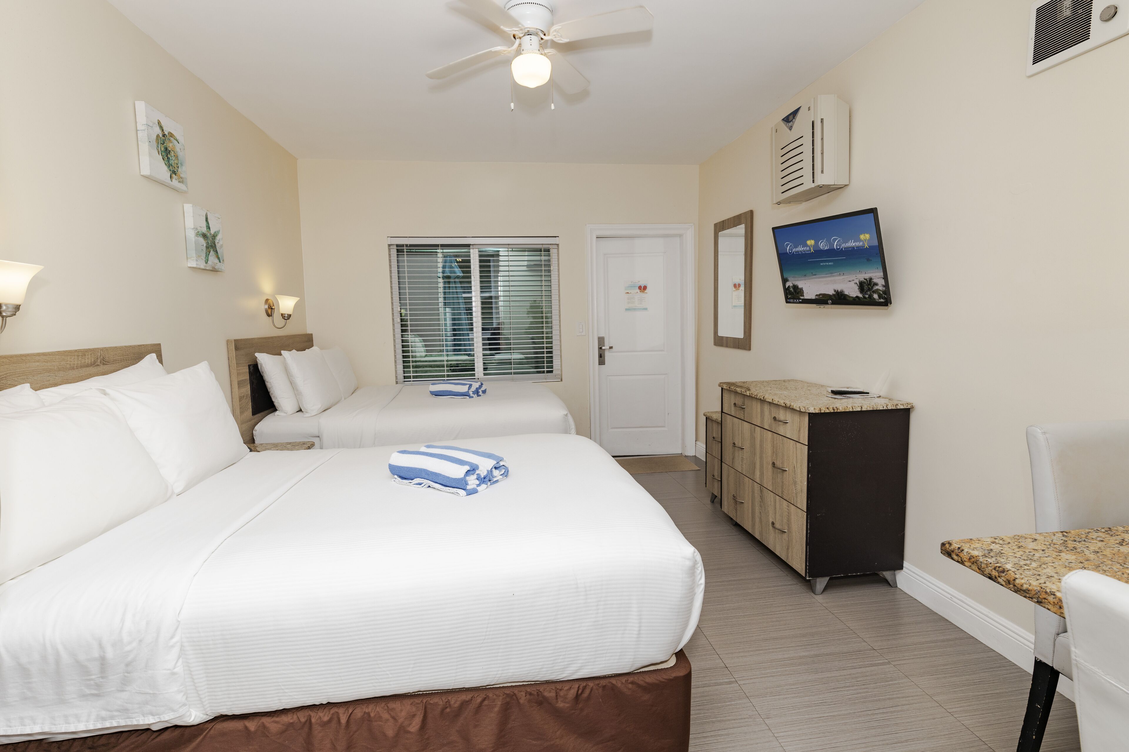 Une chambre d’hôtel avec deux lits, un bureau, une commode et un ventilateur de plafond.