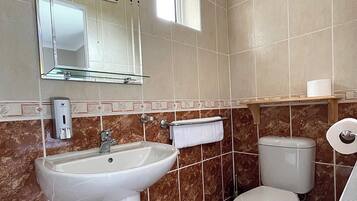 A bathroom with a sink, mirror, toilet, and a window.