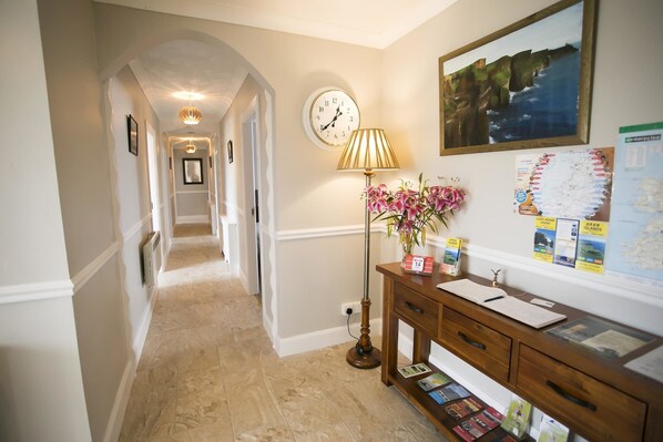 A hallway with a clock, a lamp, a desk with papers, and a framed picture on the wall. - Glasha Meadows (Doolin)