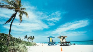 A beach with palm trees, lifeguard towers, and a clear blue sky. - Ocean Drive Villas (Hollywood)
