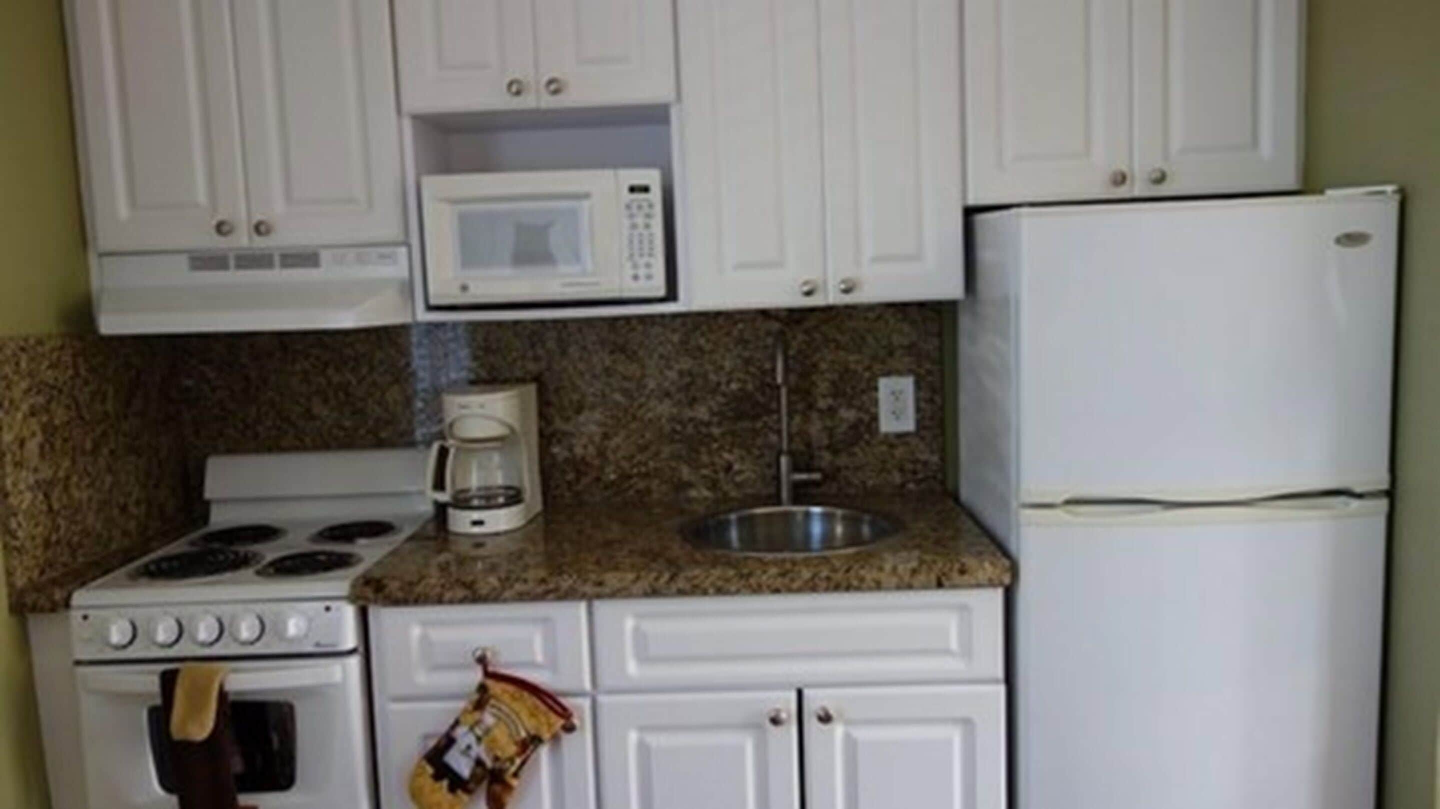 A kitchen with white cabinets, a microwave, a stove, a coffee maker, and a refrigerator.