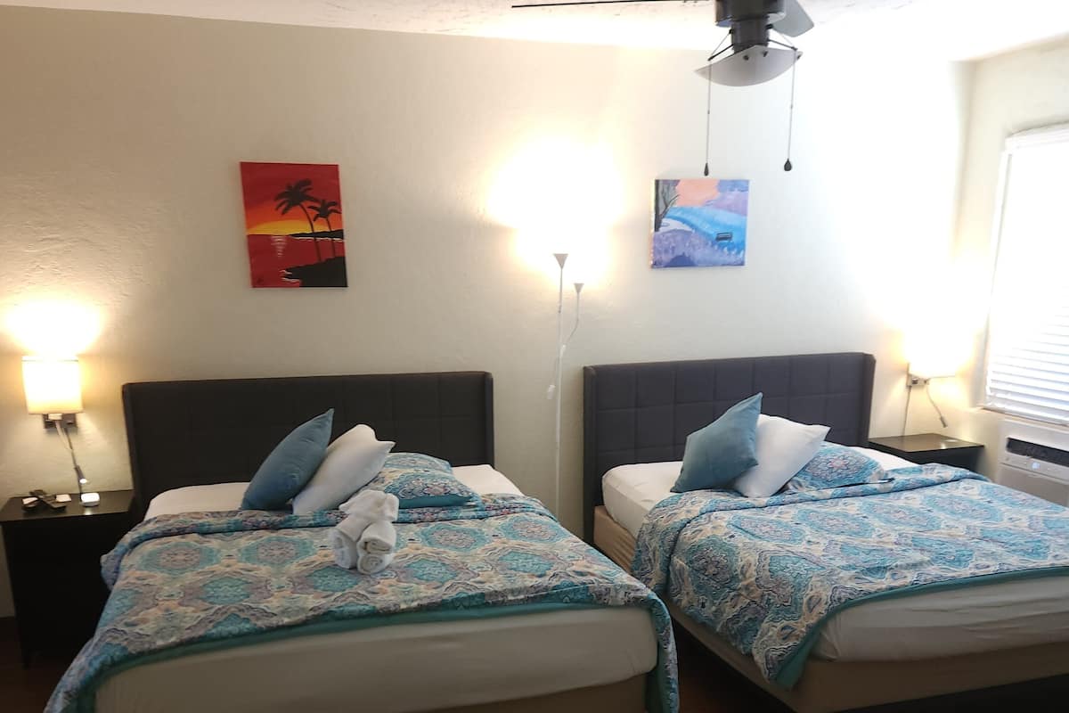 A hotel room with two beds, each with a headboard, a nightstand, and a lamp. There is a chair in the foreground.
