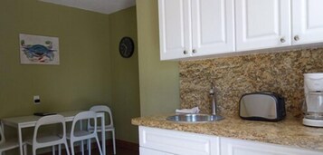 A kitchen with white cabinets, a granite countertop, a sink, a toaster, and a clock on the wall.