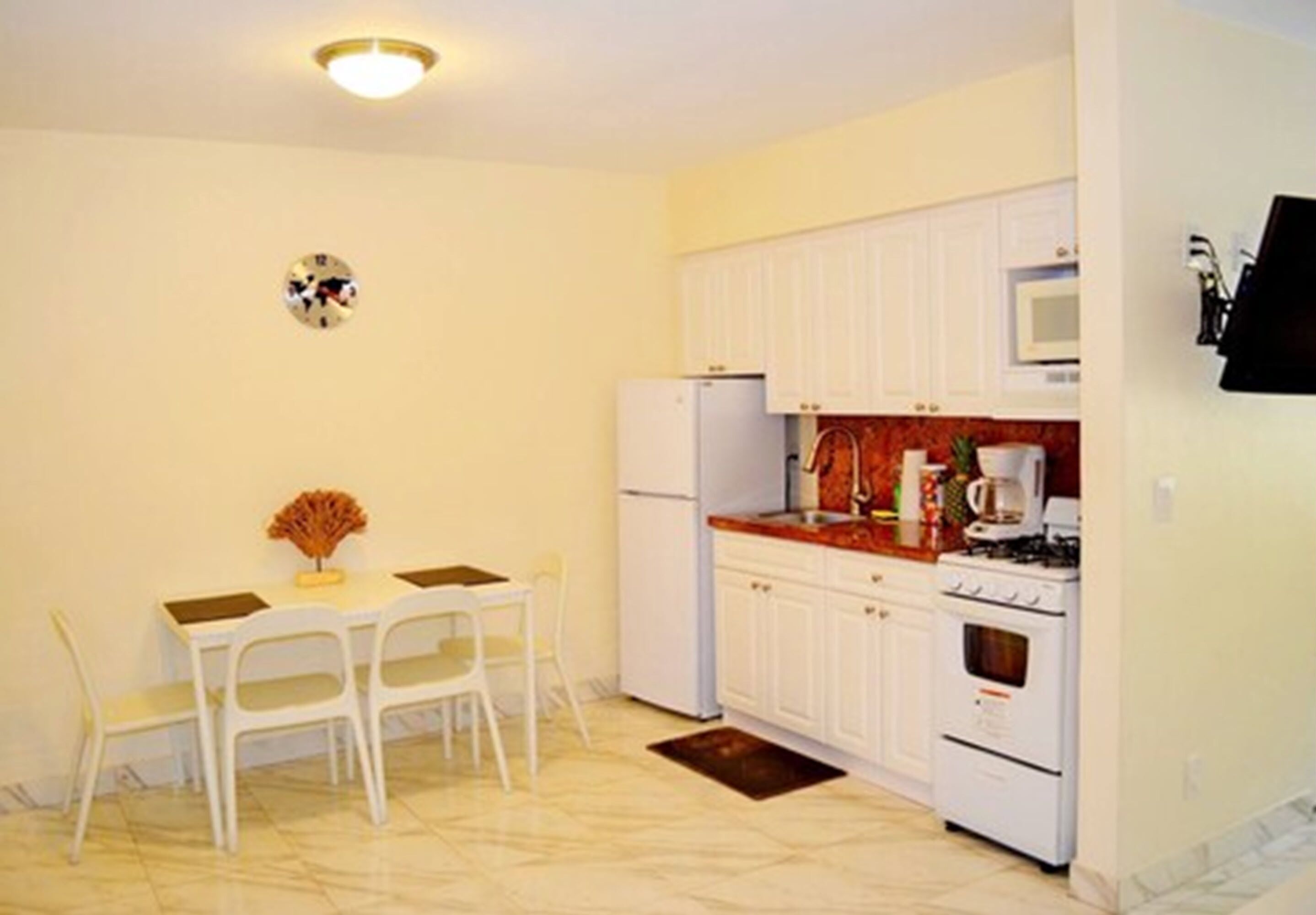 A compact kitchen with white cabinets, a white refrigerator, a microwave, and a stove. There is a dining table with chairs and a small decorative item on the table.